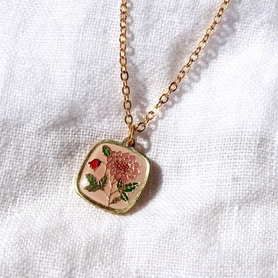 Guldhalsband med ett kvadratiskt hänge föreställande en rosa blomma.